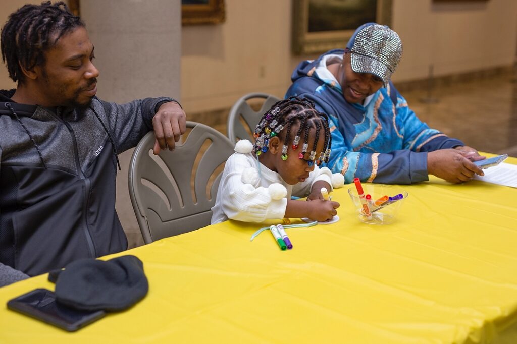A child working on a craft as her parents watch and smile at the Butler Institute of American Art.