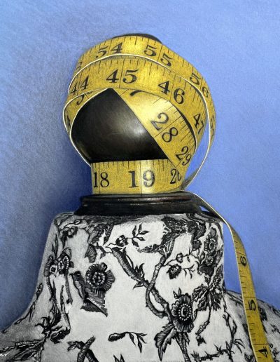 A yellow sewing tape circling a head prop, placed on a decorated pedestal in front of a blue backdrop.