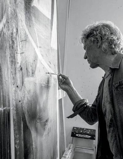 A black and white photograph of a man in the midst of painting a canvas