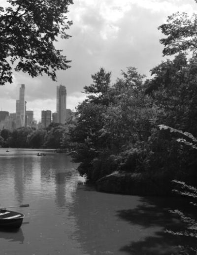 Black and white photo of water landscape with rowers in water and distant skyscrapers in background
