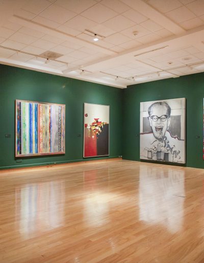 View of gallery with green walls and multiple large paintings.