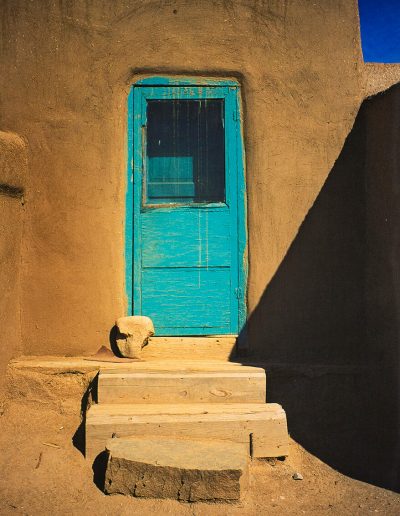 a light blue door on an sandstone wall with large blocks of stone making the stairs, a shadow is being cast from the right against the wall just before reaching the door