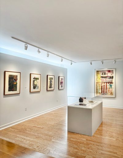 there are 2 white rectangle walls and on 1 side of the wall on the left it is 4 paintings spaced about 2 inches away from each other and on the other white wall there is another picture of mulitple color including a white and red strips. there is a square table that is in the middle of the floor that has a glass countetop with some decortive books inside of them