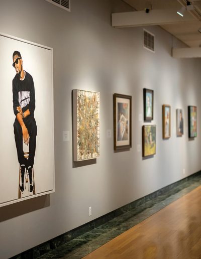 An angled photo of paintings of all shapes and sizes on the gallery wall in the 88th Midyear exhibition.