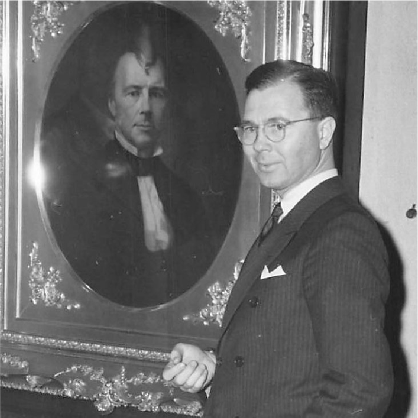 A photo of Joseph G Butler, the new Director, wearing a three piece suit and standing in front of a photo in the gallery