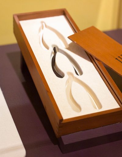 A wooden box displaying 3 wishbones of different colors (white, black and clear) Roman numeral III etched onto the box lid on top