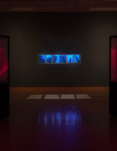 6 blurred images of a hand and forearm in motion with heavy blue filtering at a distance with two cubed displays to the left and right both with red laser lines in geometric patterns.