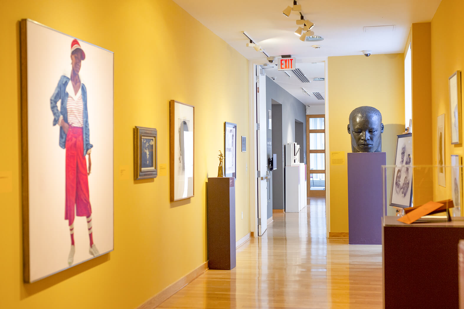 A brightly lit gallery with yellow walls and various paintings and sculptures throughout