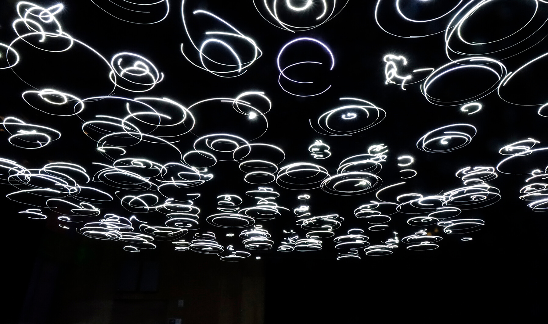 Image of lights that are spinning and seem to leave a trail of glowing light as they spin. The background is very dark, making the lights look as though they are hovering.