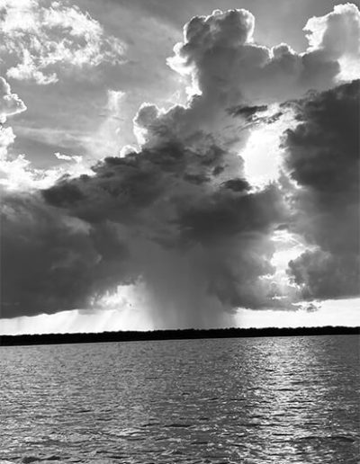 Black and white photo of rain cloud with sun shining through above a body of water